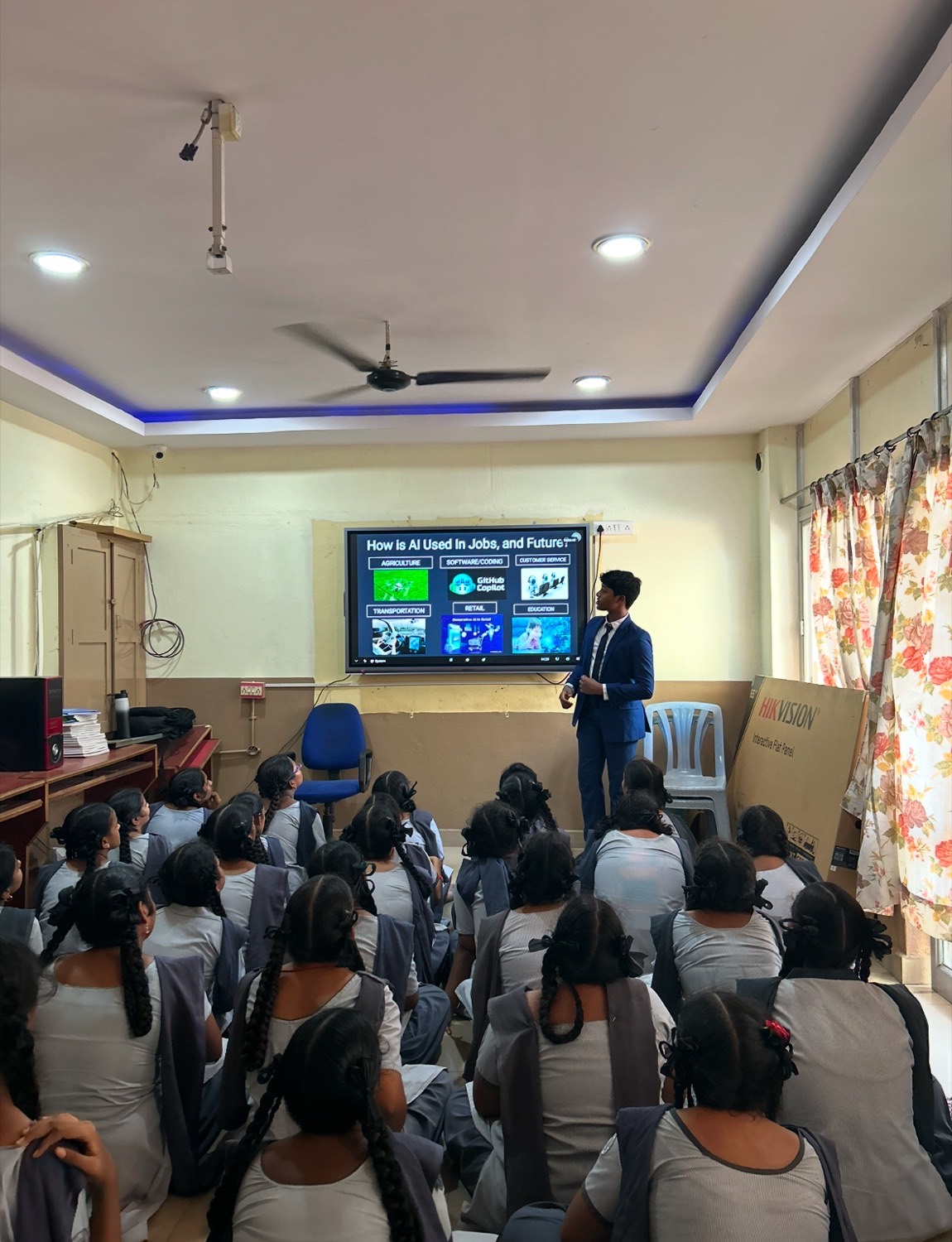 A full classroom of students in white uniforms watching the screen at the front of the room